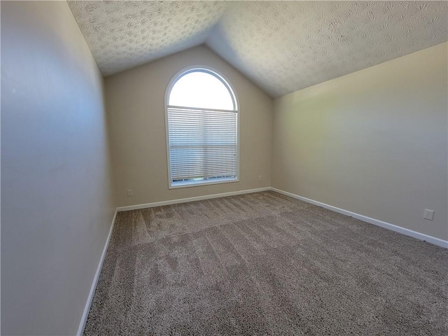 carpeted empty room with vaulted ceiling, a textured ceiling, and baseboards