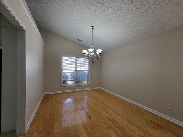 spare room featuring a chandelier, a textured ceiling, visible vents, light wood-style floors, and vaulted ceiling