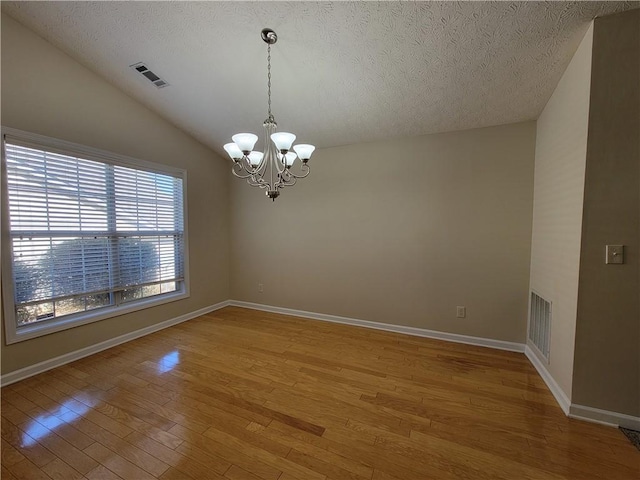 spare room featuring a notable chandelier, vaulted ceiling, a textured ceiling, and light wood-style floors