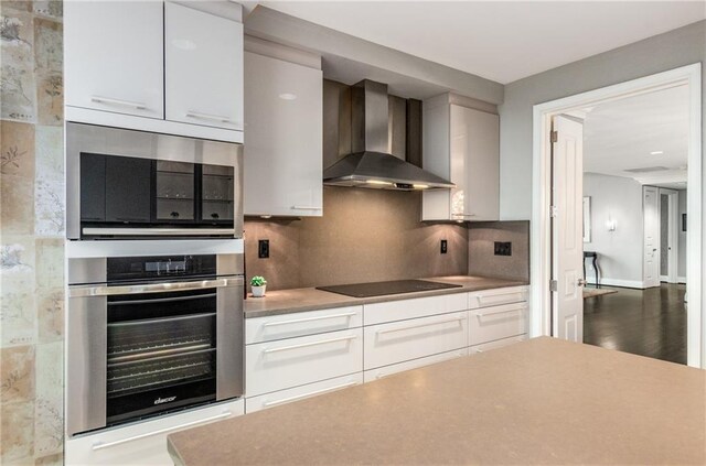 750 Park Ave NE Unit 19E, Atlanta, GA 30326 - kitchen featuring wall chimney range hood, backsplash, appliances with stainless steel finishes, white cabinets, and light countertops