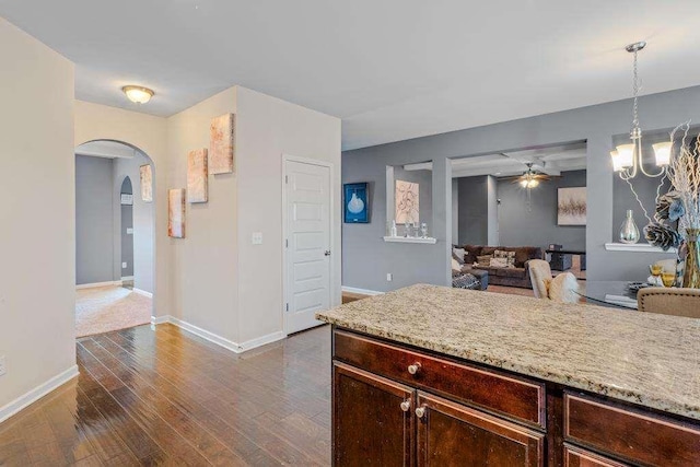 kitchen with arched walkways, decorative light fixtures, dark wood finished floors, baseboards, and ceiling fan with notable chandelier