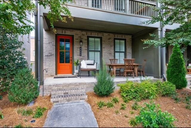view of exterior entry featuring covered porch, a balcony, and stucco siding