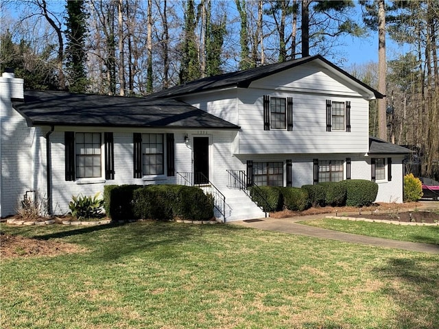 split level home featuring brick siding, a chimney, and a front yard