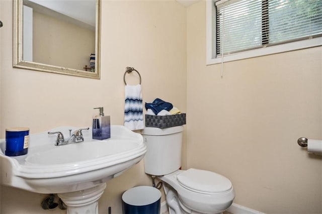 half bath with baseboards, a sink, and toilet