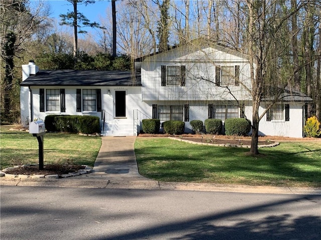 tri-level home featuring brick siding, a front lawn, and a chimney