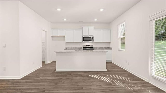 kitchen with stove, a kitchen island with sink, dark wood-type flooring, light stone counters, and white cabinetry