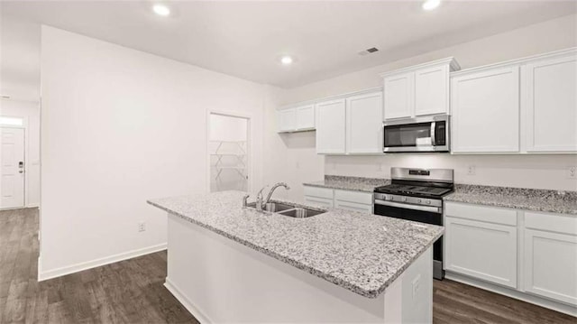 kitchen with light stone counters, stainless steel appliances, sink, white cabinetry, and an island with sink