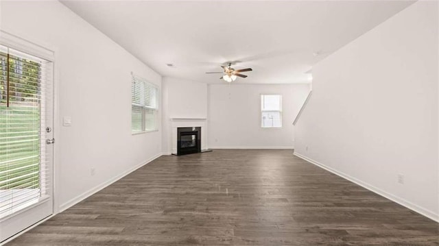 unfurnished living room with dark wood-type flooring, ceiling fan, and a healthy amount of sunlight