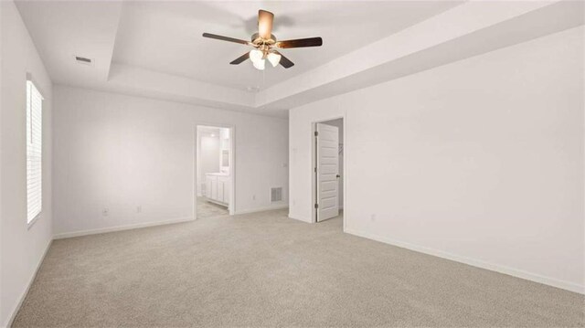 unfurnished bedroom featuring a raised ceiling, ensuite bath, ceiling fan, and light carpet