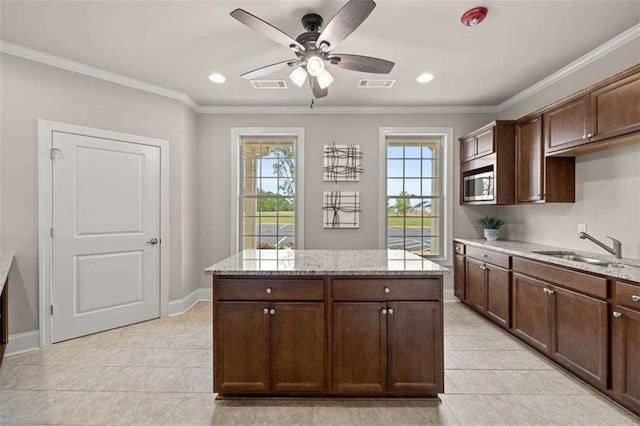 kitchen featuring stainless steel microwave, light stone countertops, sink, and dark brown cabinetry