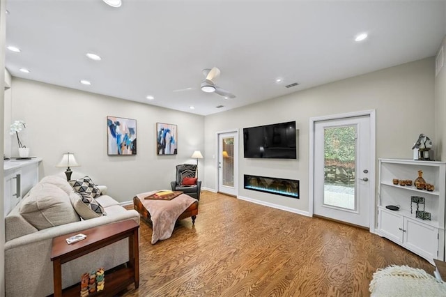 living area with a glass covered fireplace, ceiling fan, recessed lighting, and wood finished floors