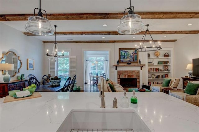 kitchen with sink, hanging light fixtures, a brick fireplace, light stone counters, and built in features