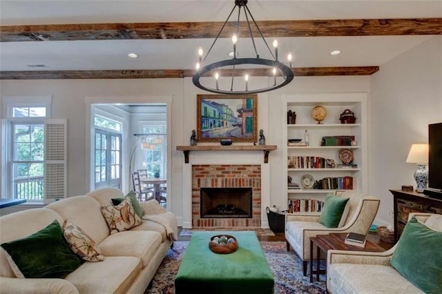 living room with beamed ceiling, a notable chandelier, built in shelves, and a brick fireplace