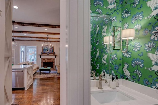 bathroom featuring a brick fireplace, vanity, an inviting chandelier, beamed ceiling, and hardwood / wood-style floors