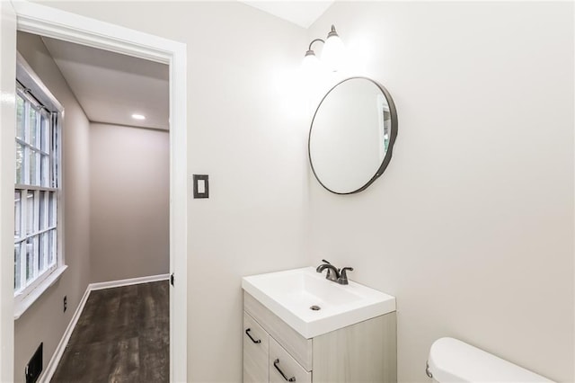 half bath with toilet, wood finished floors, vanity, baseboards, and recessed lighting