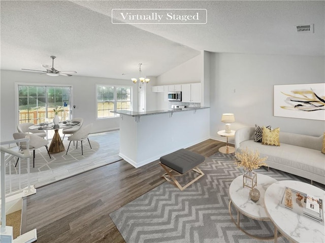 living room featuring ceiling fan with notable chandelier, wood-type flooring, a textured ceiling, and vaulted ceiling