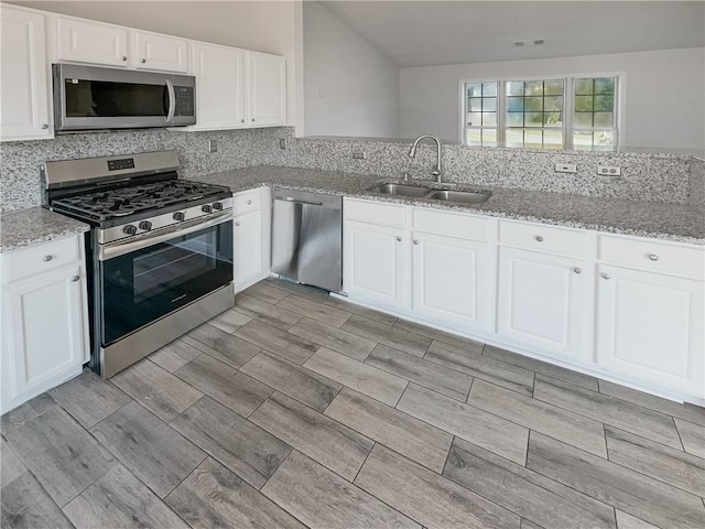 kitchen with appliances with stainless steel finishes, white cabinetry, sink, and light stone countertops