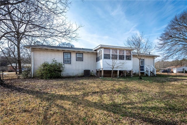 back of property featuring a sunroom, central air condition unit, and a lawn