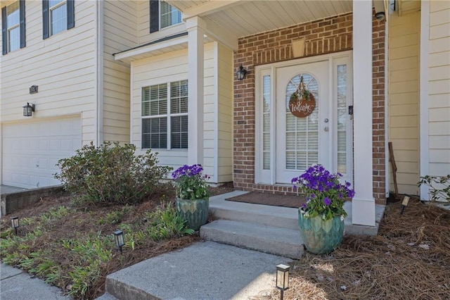 view of exterior entry with a garage, brick siding, and a porch