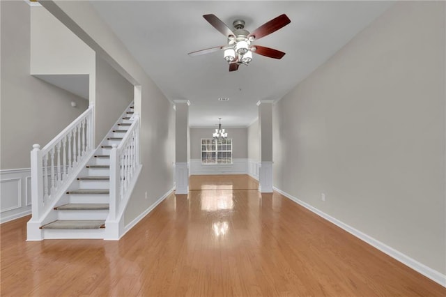 entryway with stairway, a wainscoted wall, ceiling fan with notable chandelier, wood finished floors, and a decorative wall