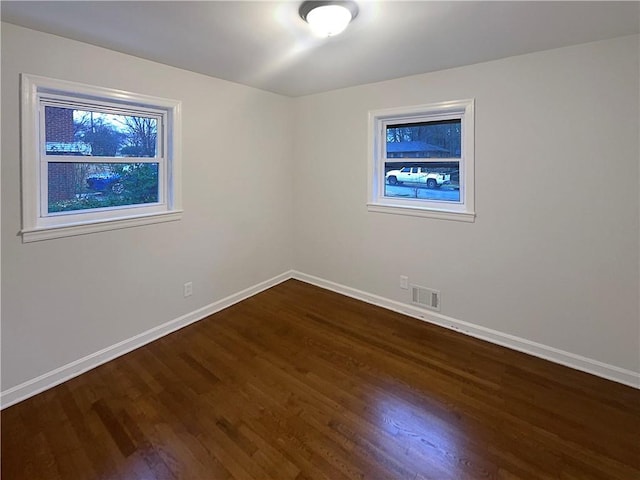 unfurnished room featuring dark wood-type flooring, visible vents, and baseboards