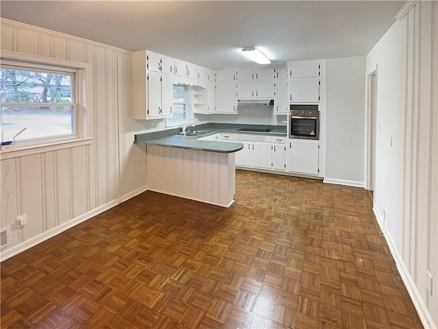 kitchen featuring dark countertops, white cabinetry, stainless steel oven, a sink, and a peninsula