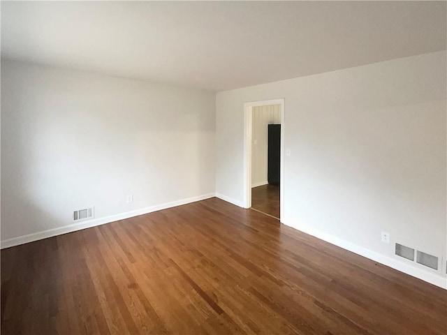 unfurnished room featuring dark wood-type flooring, visible vents, and baseboards