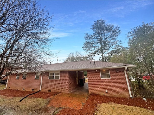 back of property featuring roof with shingles, an attached carport, crawl space, and brick siding