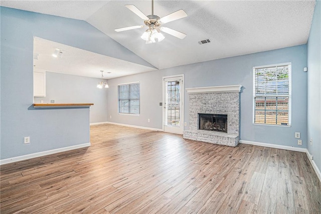 unfurnished living room with lofted ceiling, a fireplace, light hardwood / wood-style floors, a textured ceiling, and ceiling fan with notable chandelier