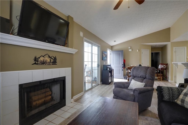 living room with light wood finished floors, a textured ceiling, vaulted ceiling, and a tiled fireplace