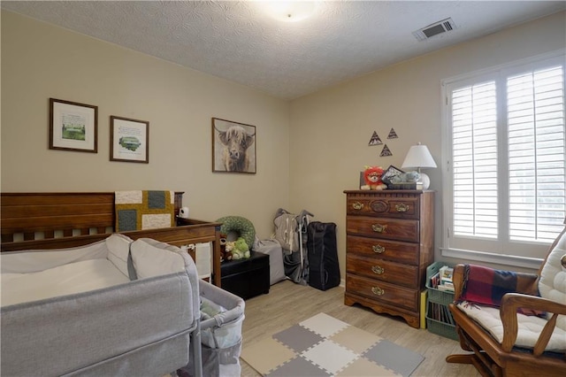 bedroom featuring light wood-style flooring, visible vents, and a textured ceiling