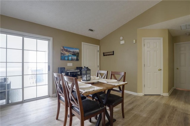 dining area with visible vents, light wood-style floors, vaulted ceiling, a textured ceiling, and baseboards