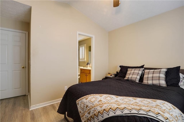 bedroom with baseboards, ensuite bath, ceiling fan, vaulted ceiling, and light wood-style floors