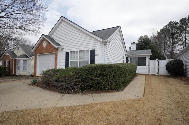 view of side of property with brick siding, a chimney, concrete driveway, a gate, and a garage