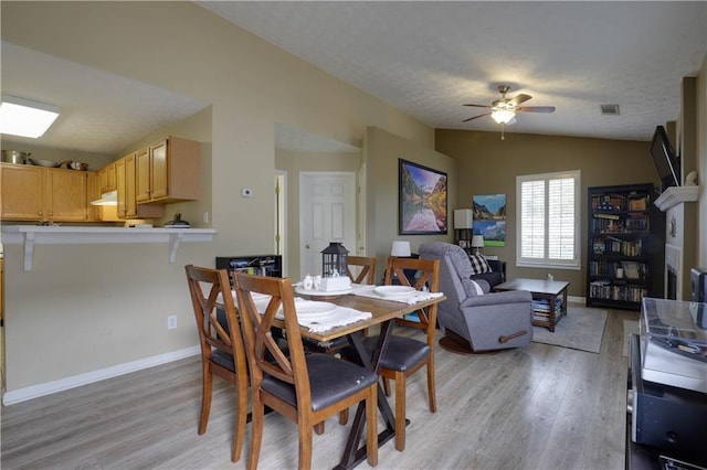 dining space with lofted ceiling, a textured ceiling, visible vents, baseboards, and light wood-style floors