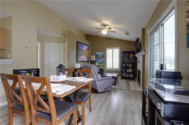 dining space featuring lofted ceiling, ceiling fan, a textured ceiling, light wood-style flooring, and visible vents