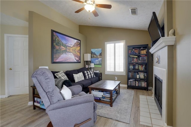 living area with visible vents, lofted ceiling, light wood-style flooring, a textured ceiling, and a fireplace