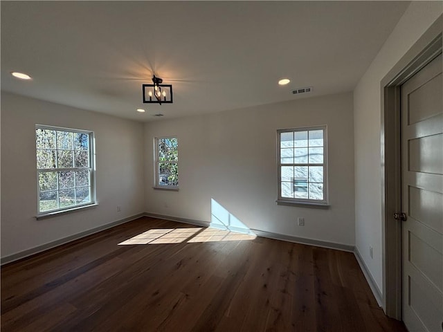 empty room featuring visible vents, baseboards, a healthy amount of sunlight, and dark wood finished floors