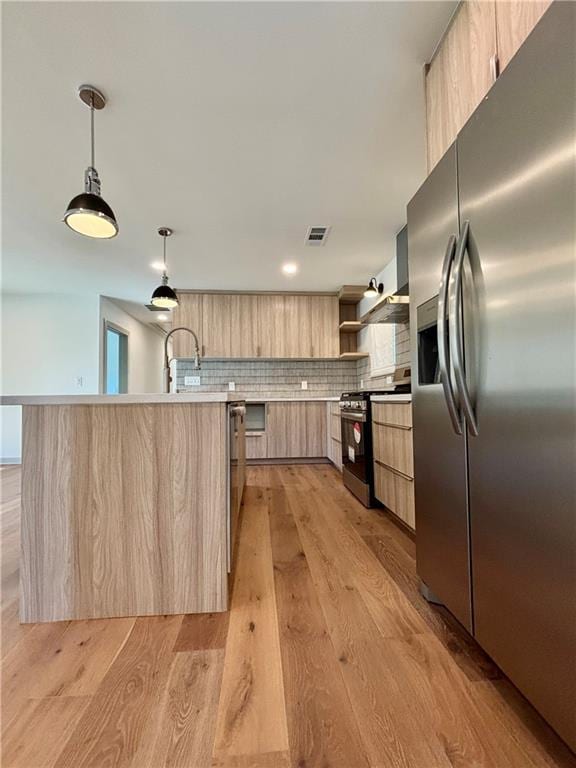 kitchen with modern cabinets, light brown cabinetry, range with gas cooktop, stainless steel fridge with ice dispenser, and light countertops