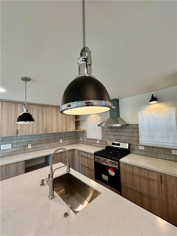 kitchen featuring wall chimney exhaust hood, modern cabinets, stainless steel gas stove, and a sink