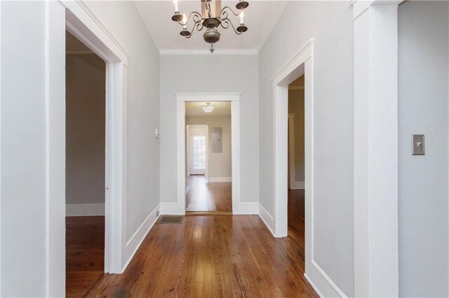 corridor with baseboards, ornamental molding, wood-type flooring, and a notable chandelier