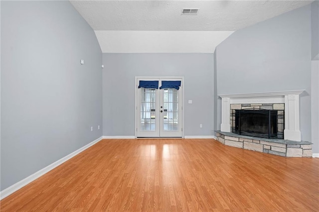 unfurnished living room featuring baseboards, vaulted ceiling, wood finished floors, and a stone fireplace