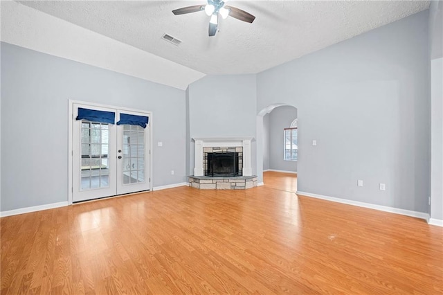 unfurnished living room with lofted ceiling, a stone fireplace, a ceiling fan, visible vents, and light wood-style floors