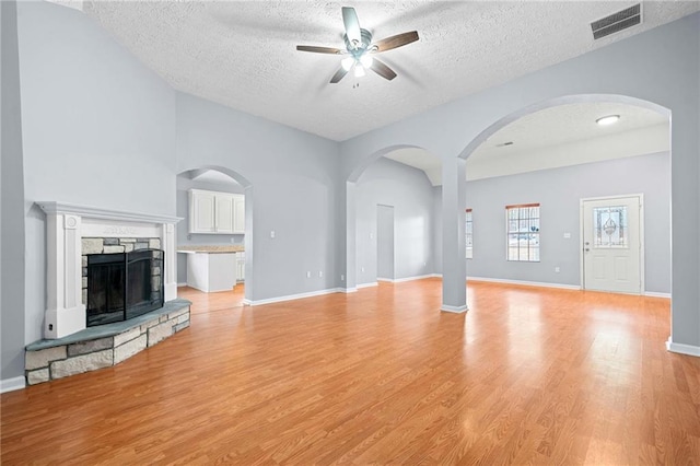 unfurnished living room featuring light wood finished floors, visible vents, a ceiling fan, and a stone fireplace