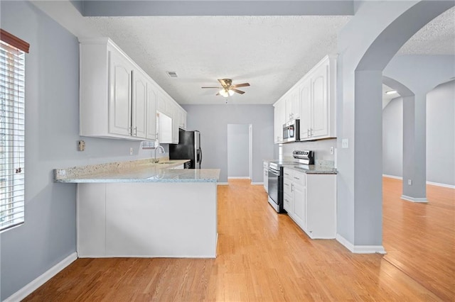 kitchen featuring arched walkways, a ceiling fan, stainless steel appliances, light wood-style floors, and a sink