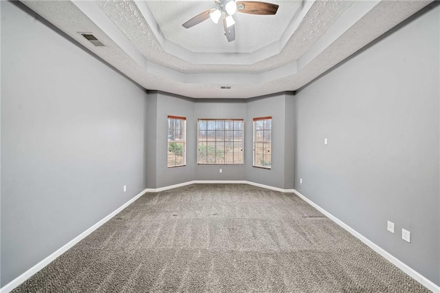 carpeted empty room with a textured ceiling, a raised ceiling, a ceiling fan, and baseboards