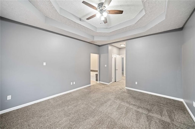 carpeted empty room featuring ceiling fan, baseboards, a raised ceiling, and a textured ceiling