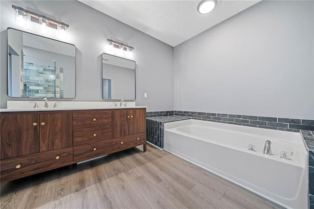 bathroom featuring double vanity, wood finished floors, a garden tub, a textured ceiling, and a sink