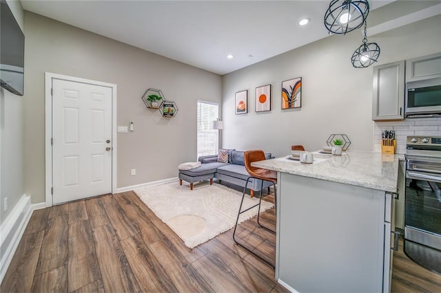 kitchen featuring a breakfast bar, gray cabinetry, decorative backsplash, appliances with stainless steel finishes, and dark wood-type flooring