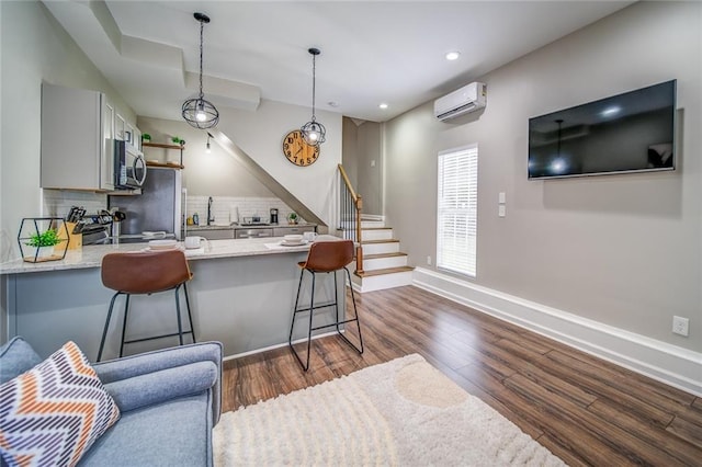 kitchen with a peninsula, a kitchen breakfast bar, a wall mounted AC, stainless steel microwave, and dark wood finished floors